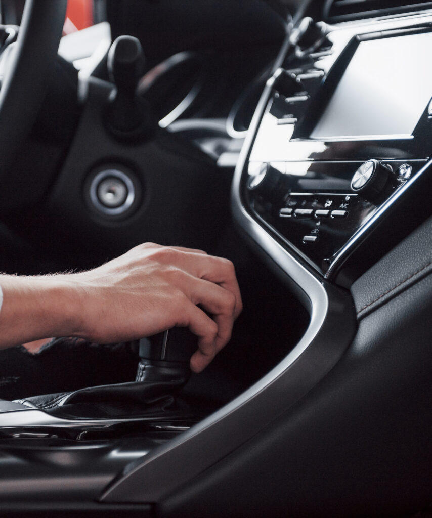 close up of a young man driving a road car holding his hand on a gearbox. a businessman rides on his car. side view, background.